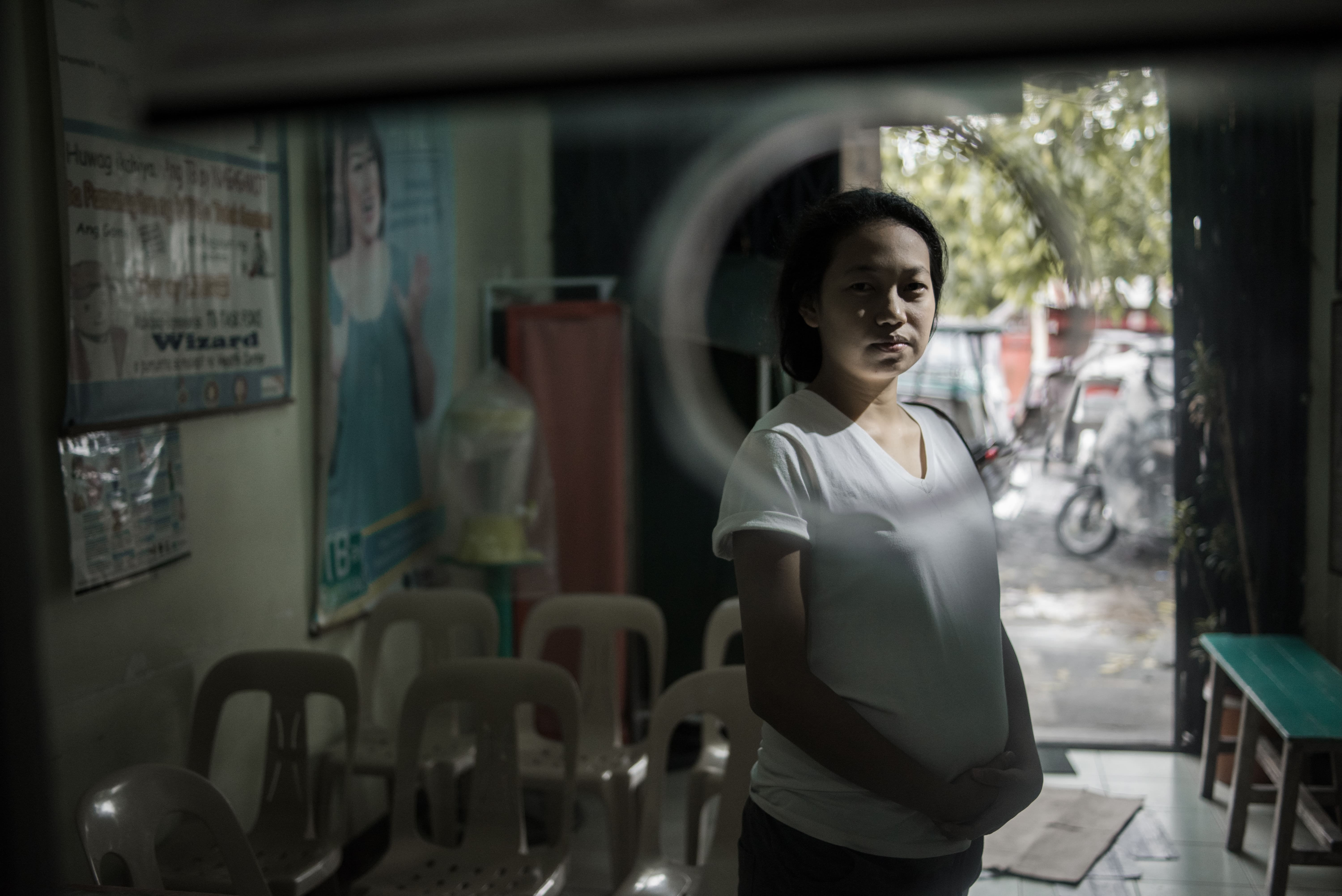 A young woman in a white t-shirts looks through a glass window.